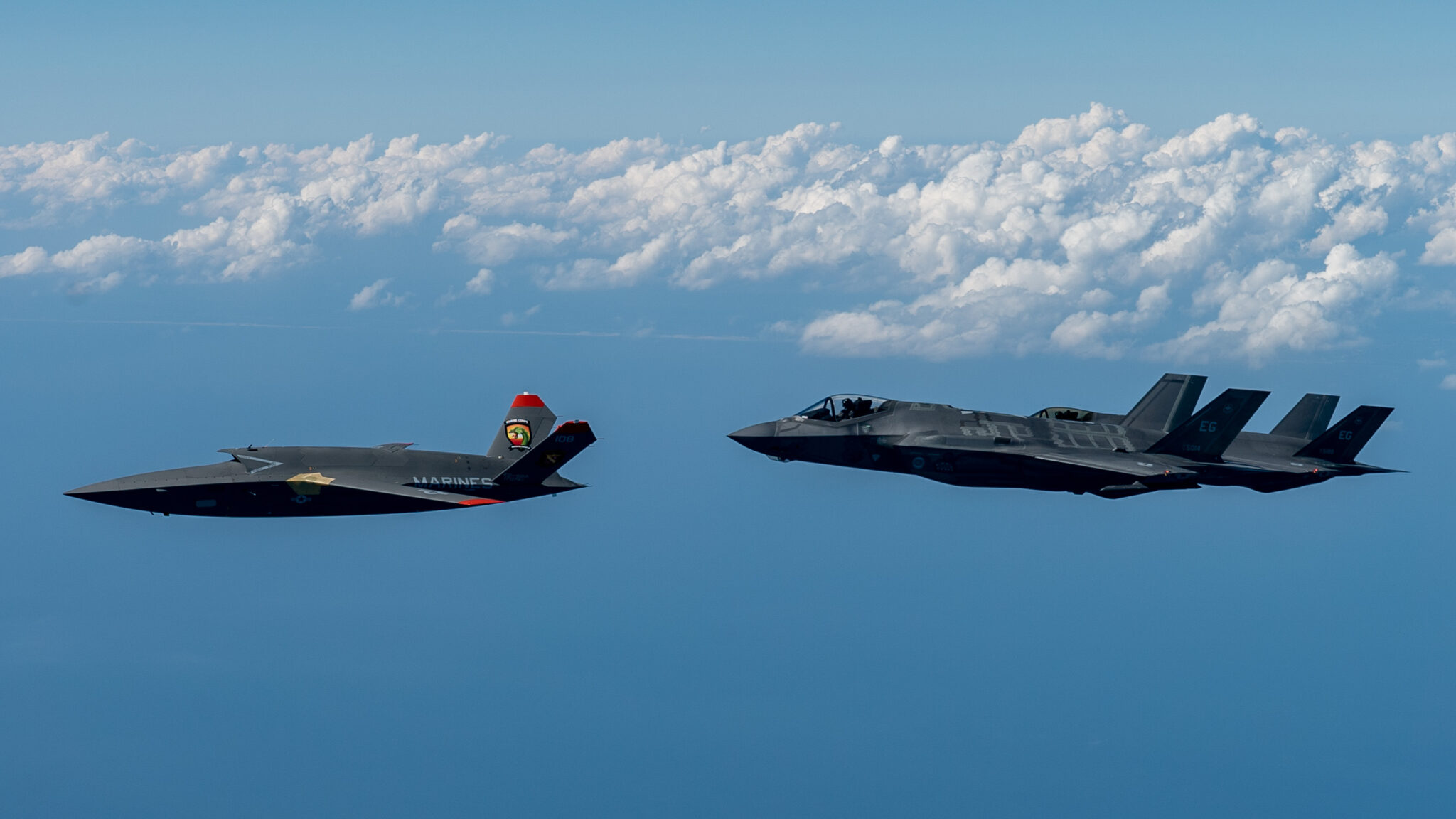 Um XQ-58A Valkyrie do US Marine Corps voa com caças F-35A Lightning II da USAF. Foto: John McRell